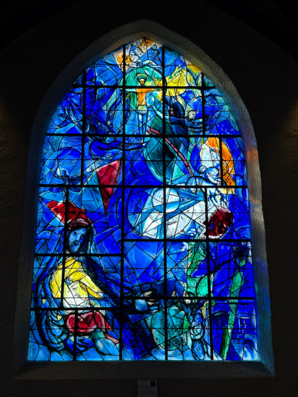 The Good Samaritan window at Union Church, designed by Marc Chagall, featuring vivid blues, reds, and greens in a depiction of the parable, including the attack, indifferent bystanders, the Good Samaritan carrying the injured man on horseback and delivering him to an inn.